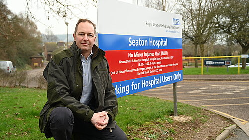 Seaton Hospital sitting Richard Foord sitting in front of the sign for Seaton Hospital