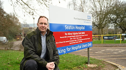 Seaton Hospital sitting Richard Foord sitting in front of the sign for Seaton Hospital