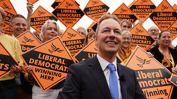 Richard Foord in front of a wall of Liberal Democrat activists holding orange diamond posters