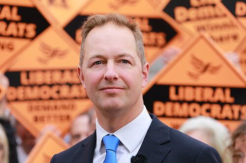 Richard Foord standing in front of signs reading "Liberal Democrats"
