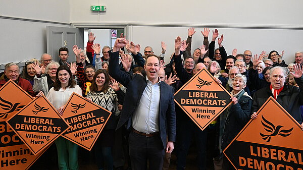 Richard Foord cheering in front of a large crowd of Liberal Democrat campaigners holding orange posters