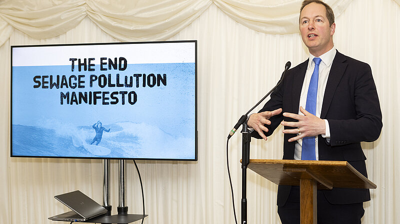Richard Foord standing next to a screen reading "The End Sewage Pollution Manifesto"