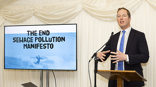 Sewage Pollution Manifesto Richard Foord standing at a podium next to a presentation slide reading "The End Sewage Pollution Manifesto"