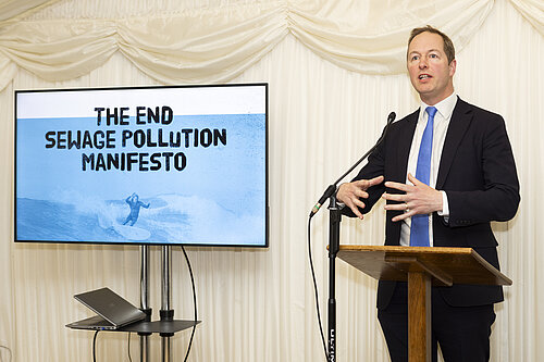 Richard Foord standing next to a presentation slide reading "The End Sewage Pollution Manifesto"