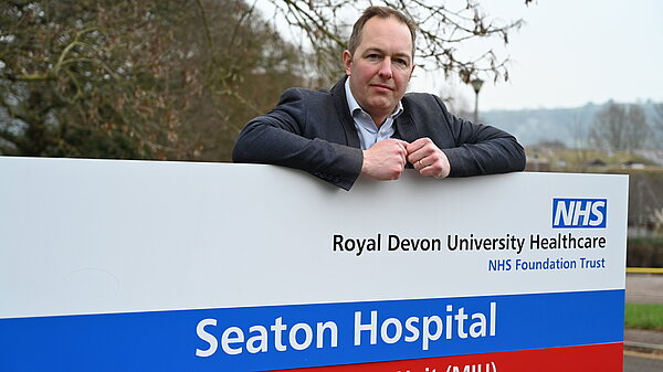 Richard Food leaning on the Seaton Hospital sign