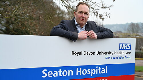 Seaton Hospital behind sign Richard Foord standing behind the sign for Seaton Hospital